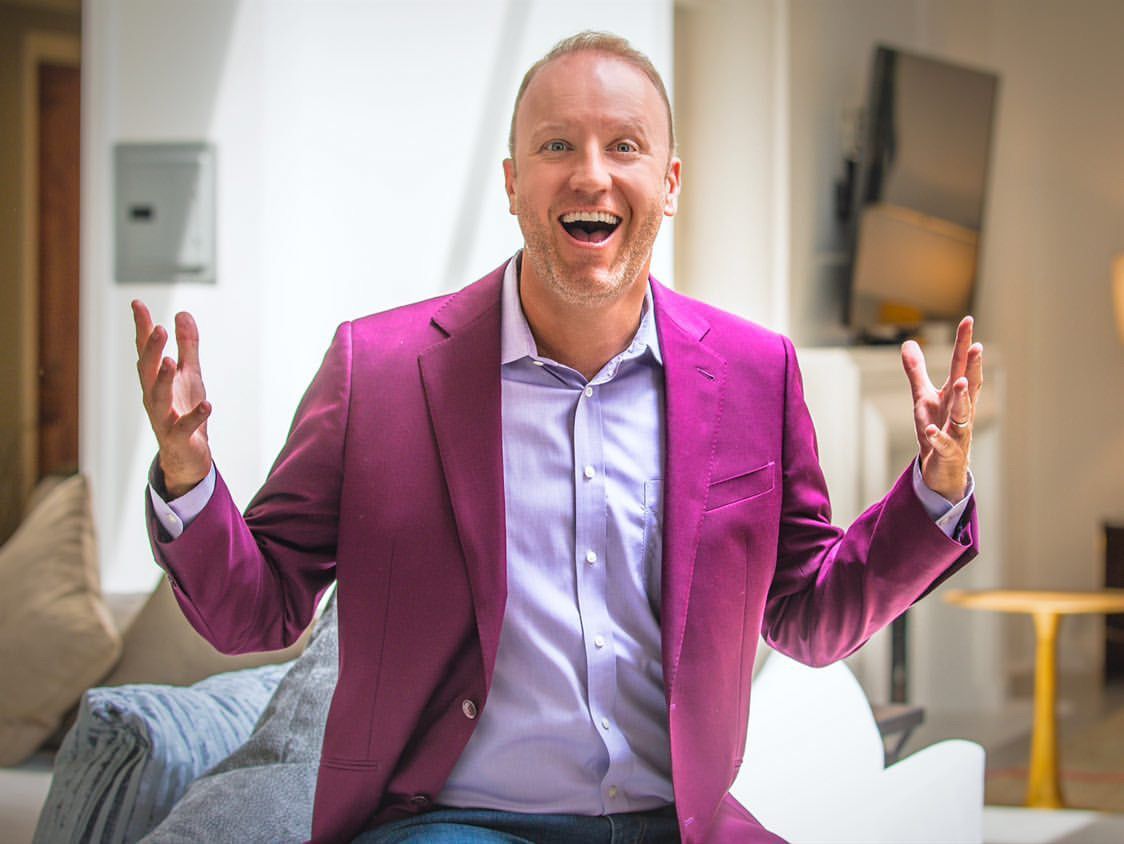 Darren Marble in a magenta blazer, arms open, mid-laugh